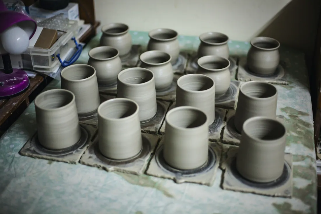 Piezas de cerámica sin cocer secándose alineadas sobre una superficie de taller